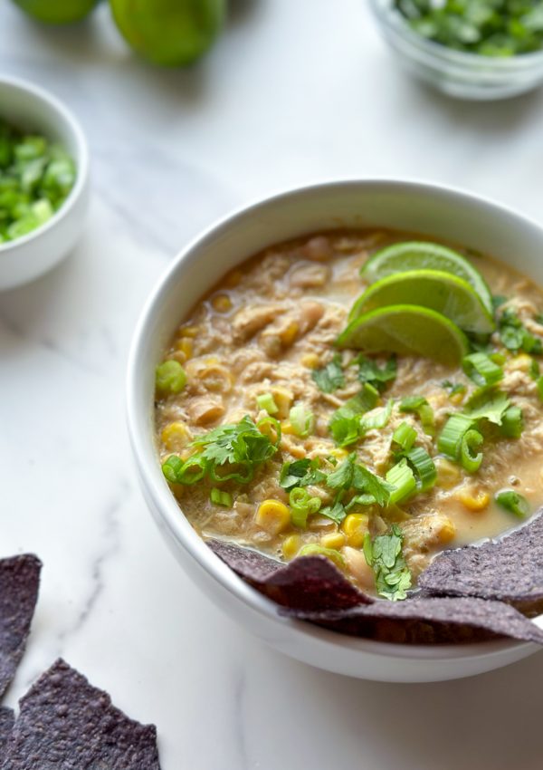 a bowl of white chicken chili next to chips and toppings