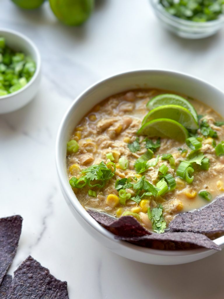 a bowl of white chicken chili next to chips and toppings