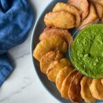 a plate full of Afghan Pakawra, which is a veggie fritter. this one is potato with a bowl of cilantro chutney