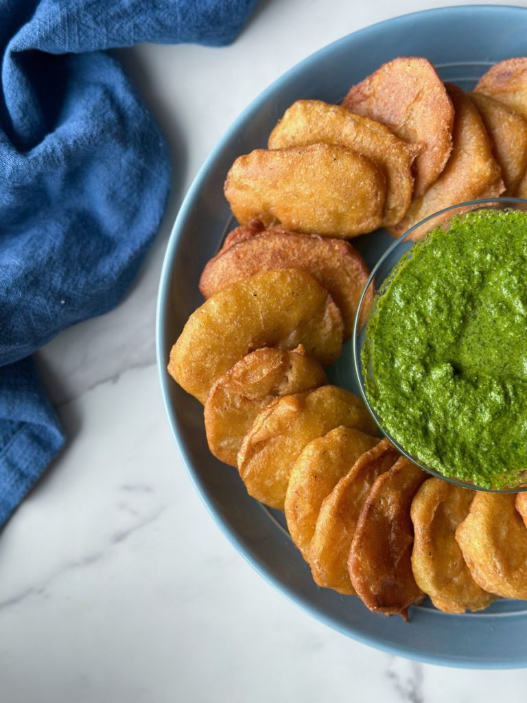 a plate full of Afghan Pakawra, which is a veggie fritter. this one is potato with a bowl of cilantro chutney