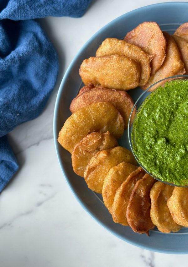 a plate full of Afghan Pakawra, which is a veggie fritter. this one is potato with a bowl of cilantro chutney