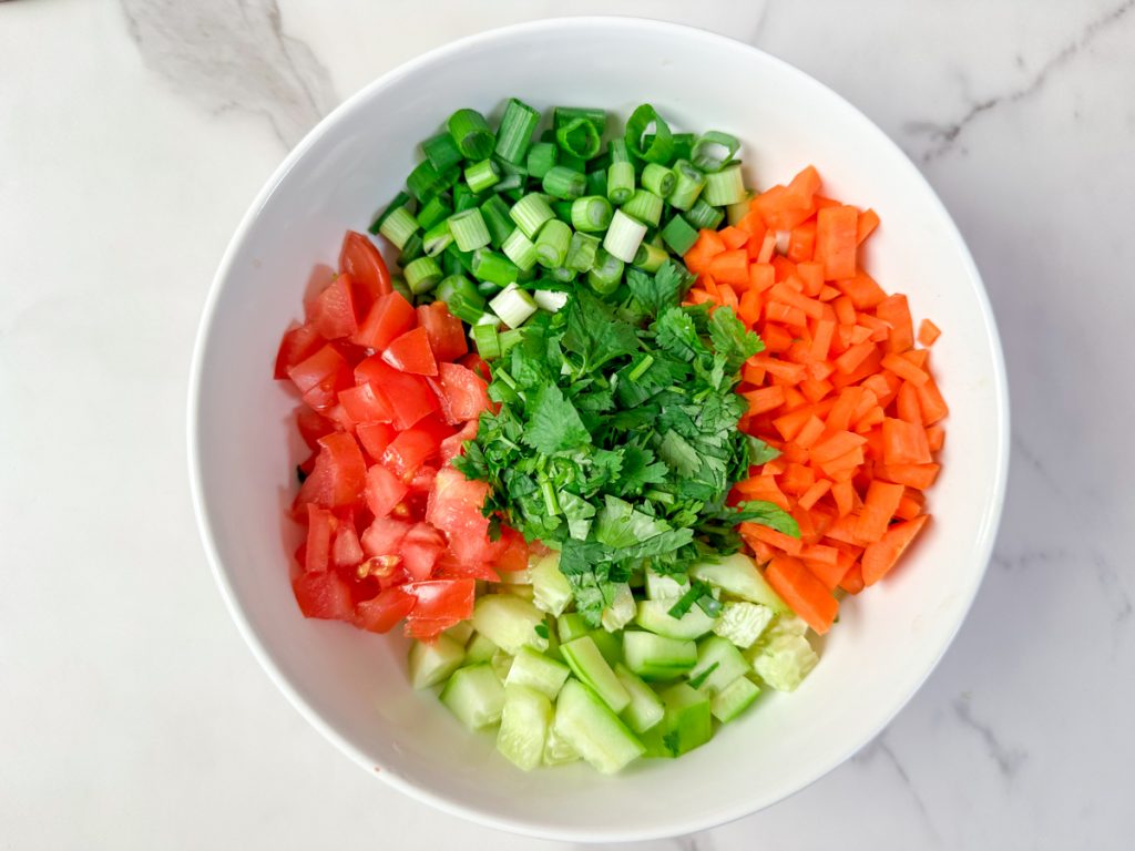 a bowl of salata. cucumbers. carrots. green onions. tomatoes and cilantro