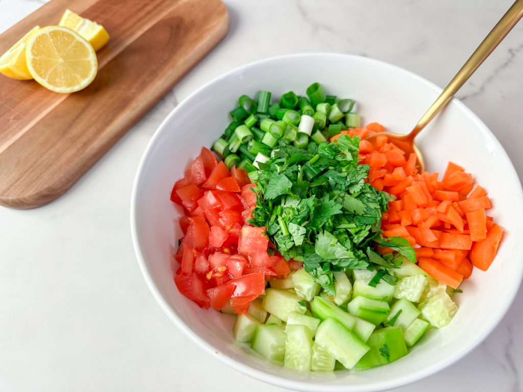 a bowl of salata. cucumbers. carrots. green onions. tomatoes and cilantro