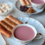 a beautiful cup of Sheer Chai, an afghan pink tea with milk. surrounded by plates of raising and walnuts and afghan bread, along with qaimagh