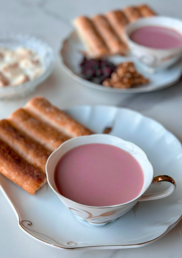 a beautiful cup of Sheer Chai, an afghan pink tea with milk. surrounded by plates of raising and walnuts and afghan bread, along with qaimagh