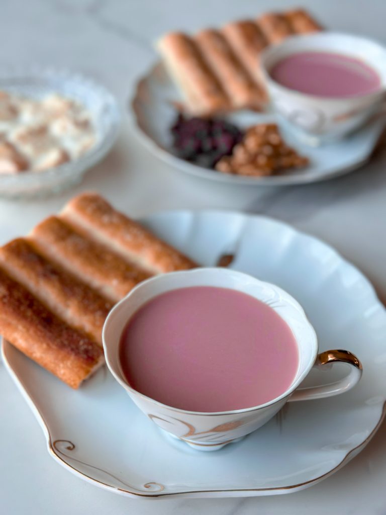 a beautiful cup of Sheer Chai, an afghan pink tea with milk. surrounded by plates of raising and walnuts and afghan bread, along with qaimagh