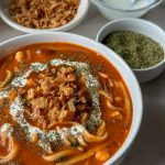 a bowl of afghan spaghetti called Aush with two bowls and some dried mint next to it