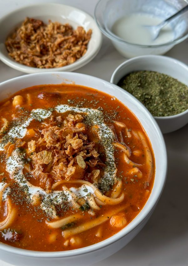 a bowl of afghan spaghetti called Aush with two bowls and some dried mint next to it