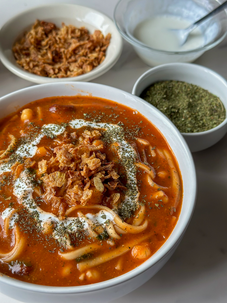 a bowl of afghan spaghetti called Aush with two bowls and some dried mint next to it